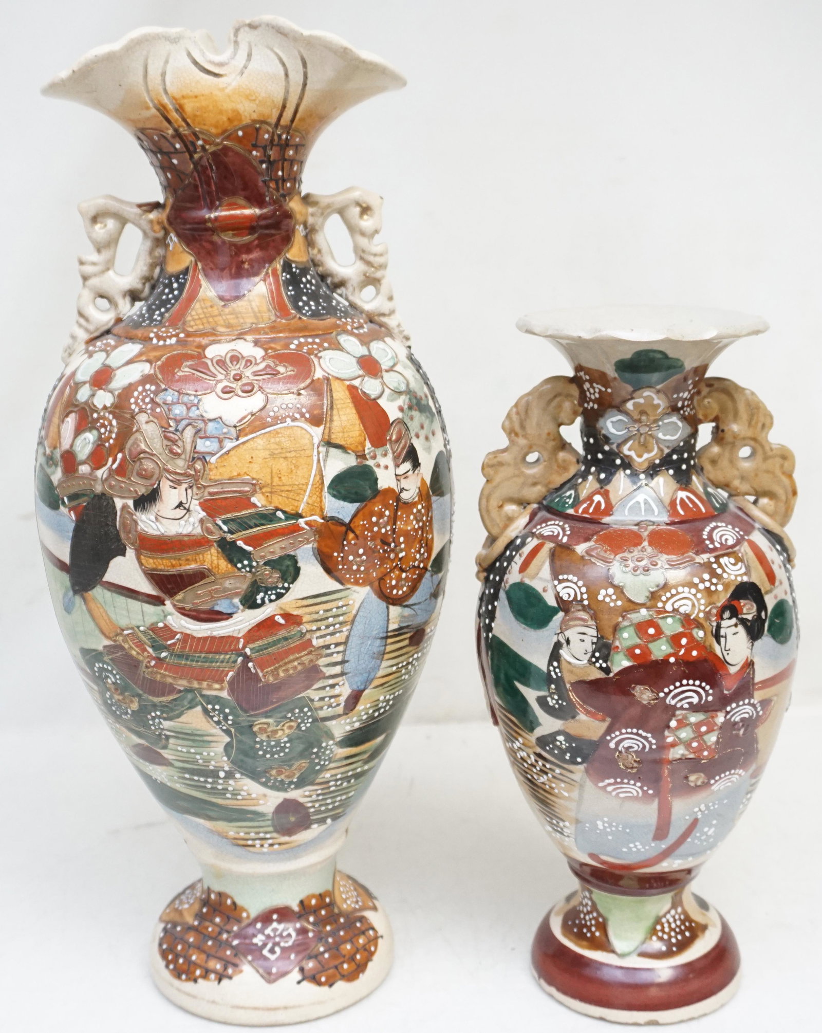 2 JAPANESE POTTERY SATSUMA VASES: Two Japanese Pottery Moriage Satsuma Vases. Both heavily hand enameled with figures and stylized flora, having applied pierced handles. Meiji Period, late 19th, early 20th c. Largest with Samurai, the