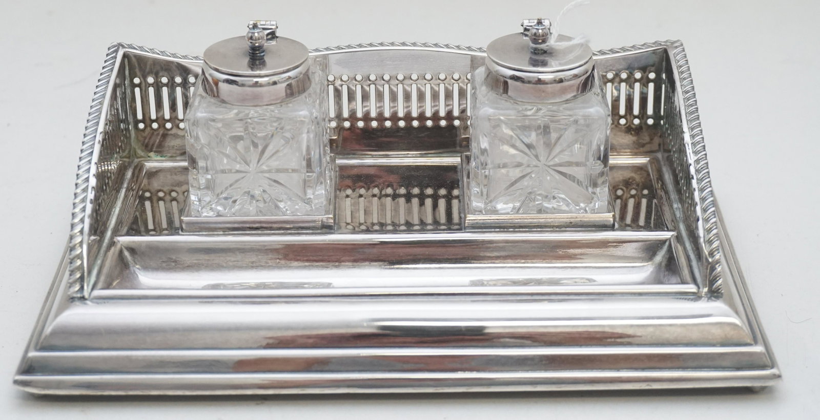 ENGLISH SILVER PLATE DOUBLE INKWELL: A vintage English silverplate double inkwell. This inkwell features a pierced gallery edge with two glass inkwells, a place to hold a quill or pen, and ball feet. Measures 8 1/4"x5 1/4"x3 1/2". Weight