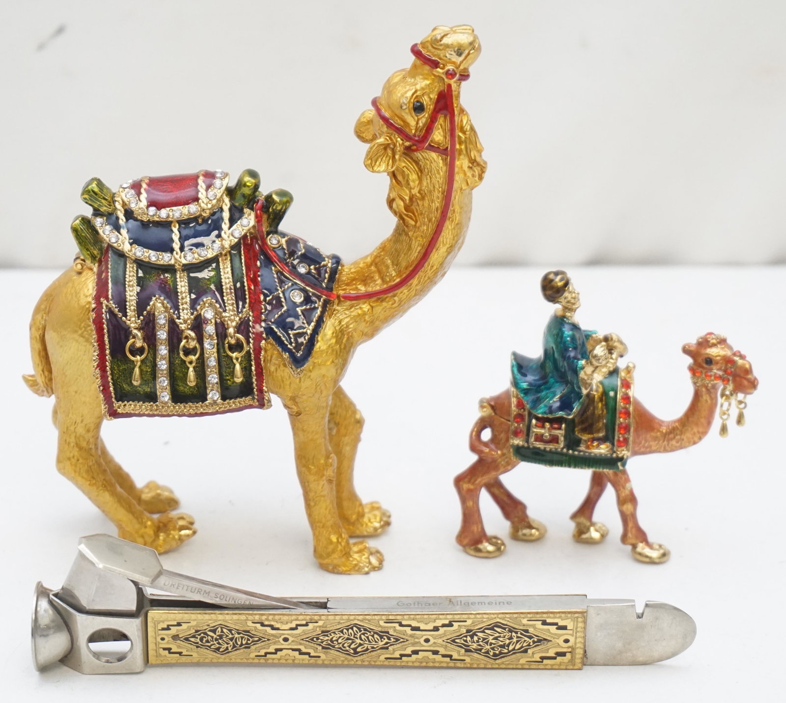 3 pc CAMEL BOXES + CIGAR CUTTER: 1 - Antique German steel cigar cutter with Niello Handle 5 3/4". 2&3 - Enamel and Rhinestone Camel boxes in the manner of Jay Strongwater. 5" and 3" tall. Weight on all 1 pd 8 oz. PROVENANCE: A Privat