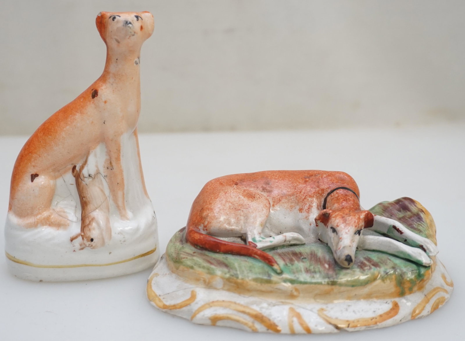 2 OLD STAFFORDSHIRE 19th c GREYHOUNDS: 2 Original Old Staffordshire 19th c. Greyhounds. 1- Reclining with head down, old repair (glue) to base 4 1/4" long. 2- Sitting with hare 3 3/4", old hairlines by hare. Weight combined 8 oz. PROVENANC