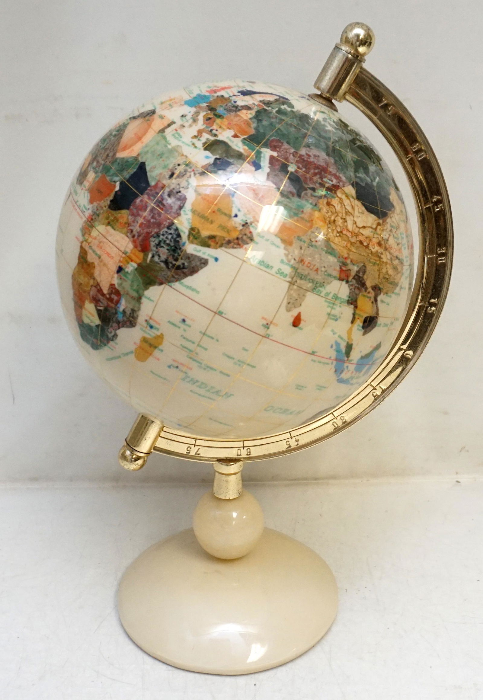 CONTEMPORARY INLAID SEMI PRECIOUS STONE GLOBE: Fine Semi Precious Gemstone Inlaid Desktop Globe.inlaid with semi-precious gemstones including jasper, jade, abalone and others. Gold lined latitude and longitude markers. Cream Onyx Base. Measures 15