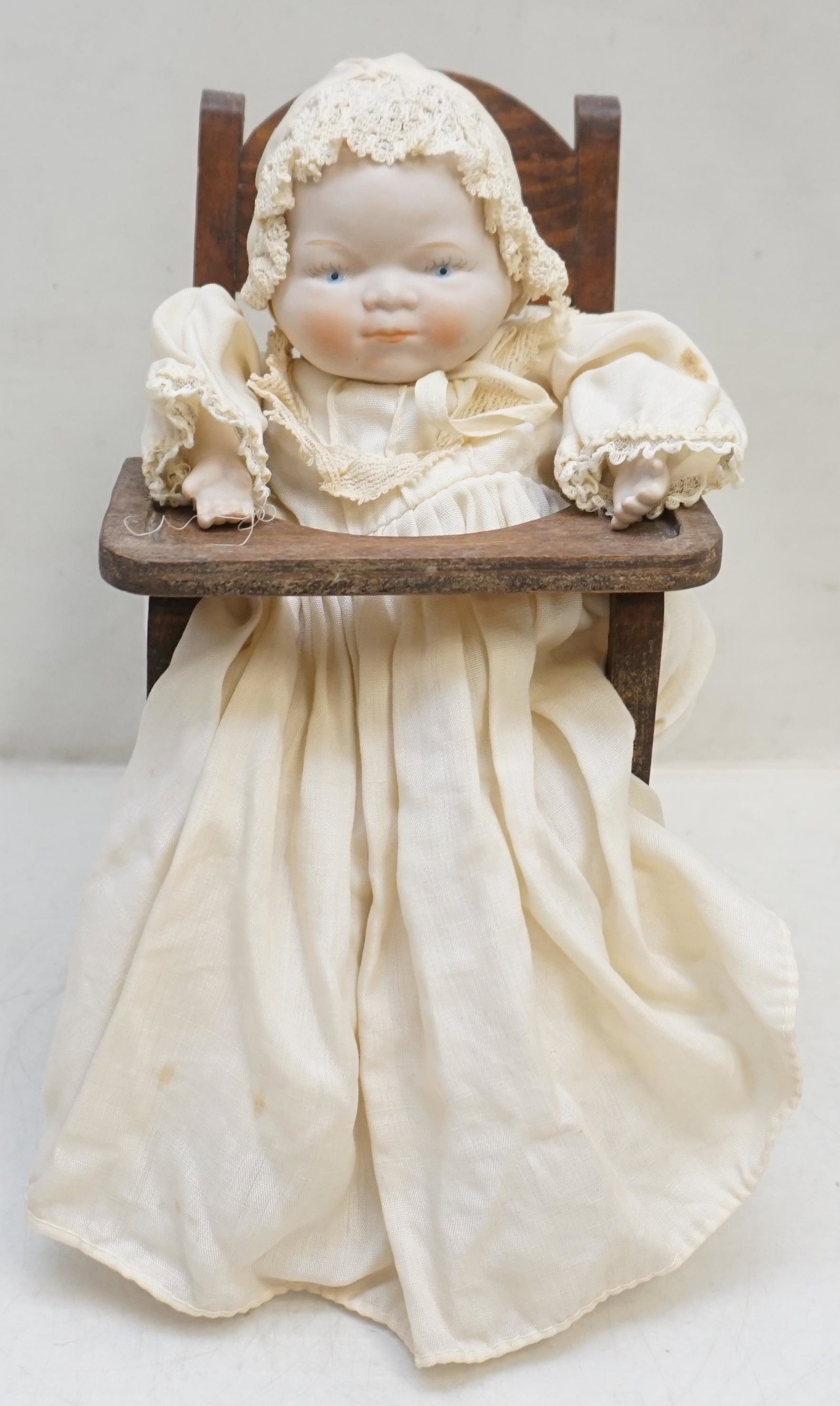 ANTIQUE PORCELAIN BISQUE BABY DOLL: Antique / Vintage Porcelain Bisque Grace Putnam Style Baby Doll in Wooden High Chair. Doll 10". Chair 10". Weight on all 13 oz. PROVENANCE: A Private Charleston SC Estate.