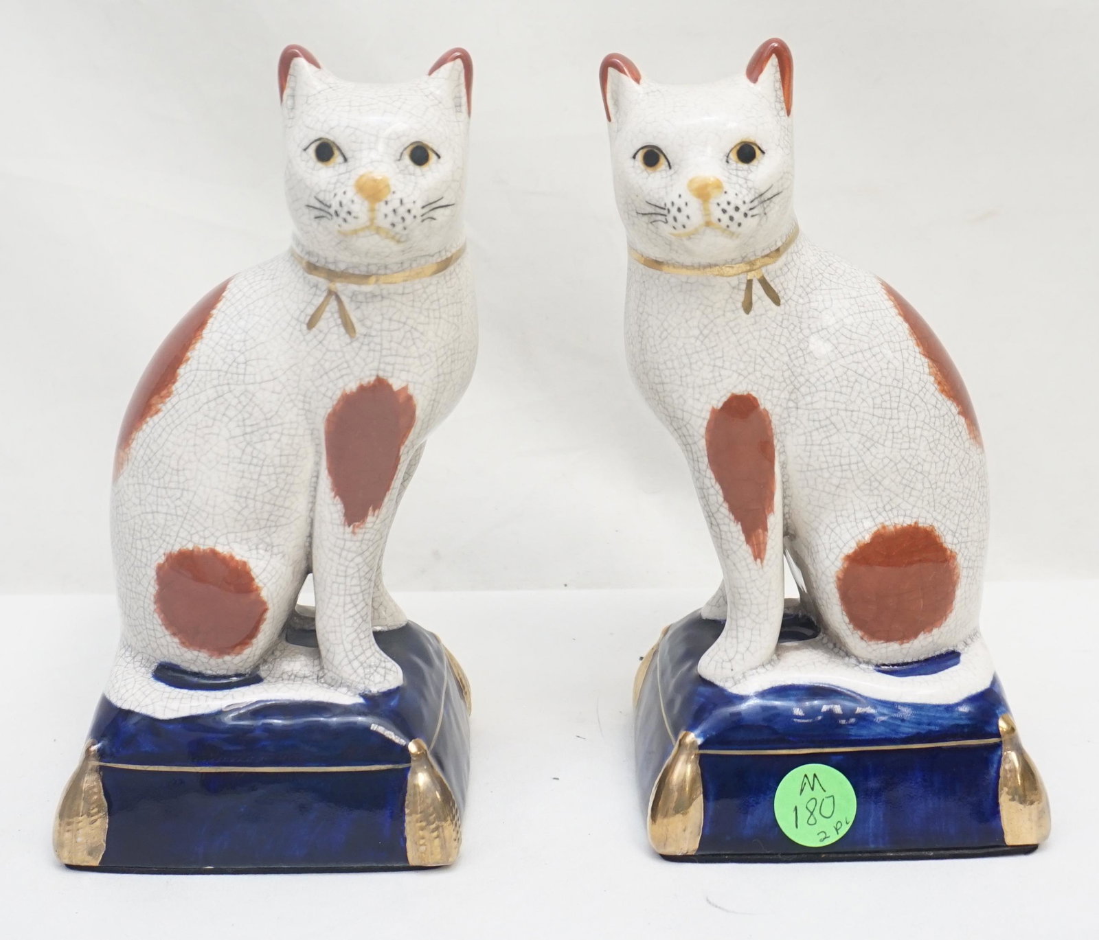 PAIR SEATED STAFFORDSHIRE CATS: Pair of 20th c. English Staffordshire Seated Cats. Cats with freestanding front legs seated on blue pillows with gilt trim. The cats have gilt ribbons and black spatter spots. Each 7 1/4 "h. Weight 2 