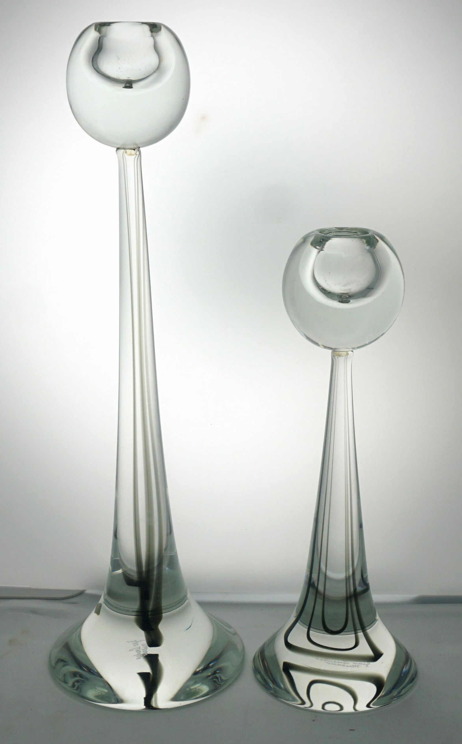 2 MID CENTURY GINO CENEDESE MURANO GLASS CANDLESTICKS: Set of two graduated Murano Mid Century Modern art glass signed candlesticks. Signed Gino Cenedese, these modernist style candlesticks feature a black swirl and clear glass bulbous design on tapered s