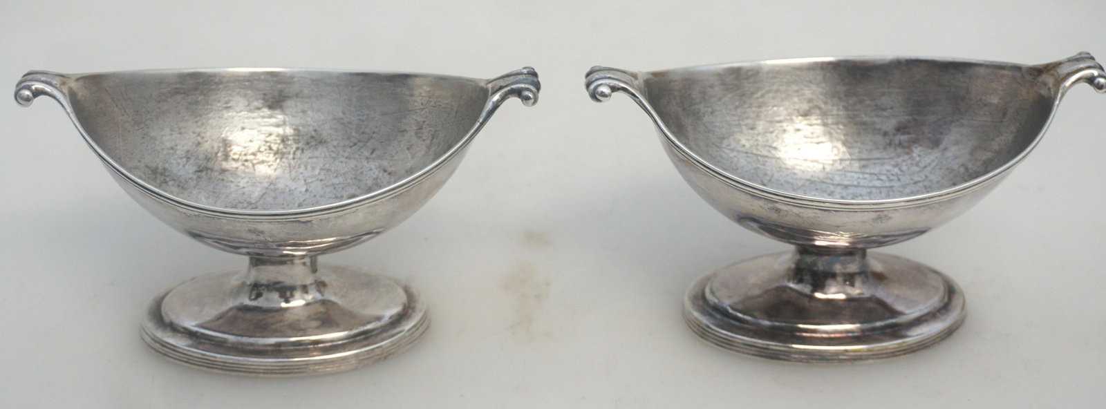 PAIR 18TH c STERLING SALTS PETER & ANN BATEMAN: English George III sterling silver pair of footed open salt dishes, having lobed, slightly pointed oval bowls with scroll handles. Made by Peter & Ann Bateman, London, in the year 1797.Measures 4 1/2"