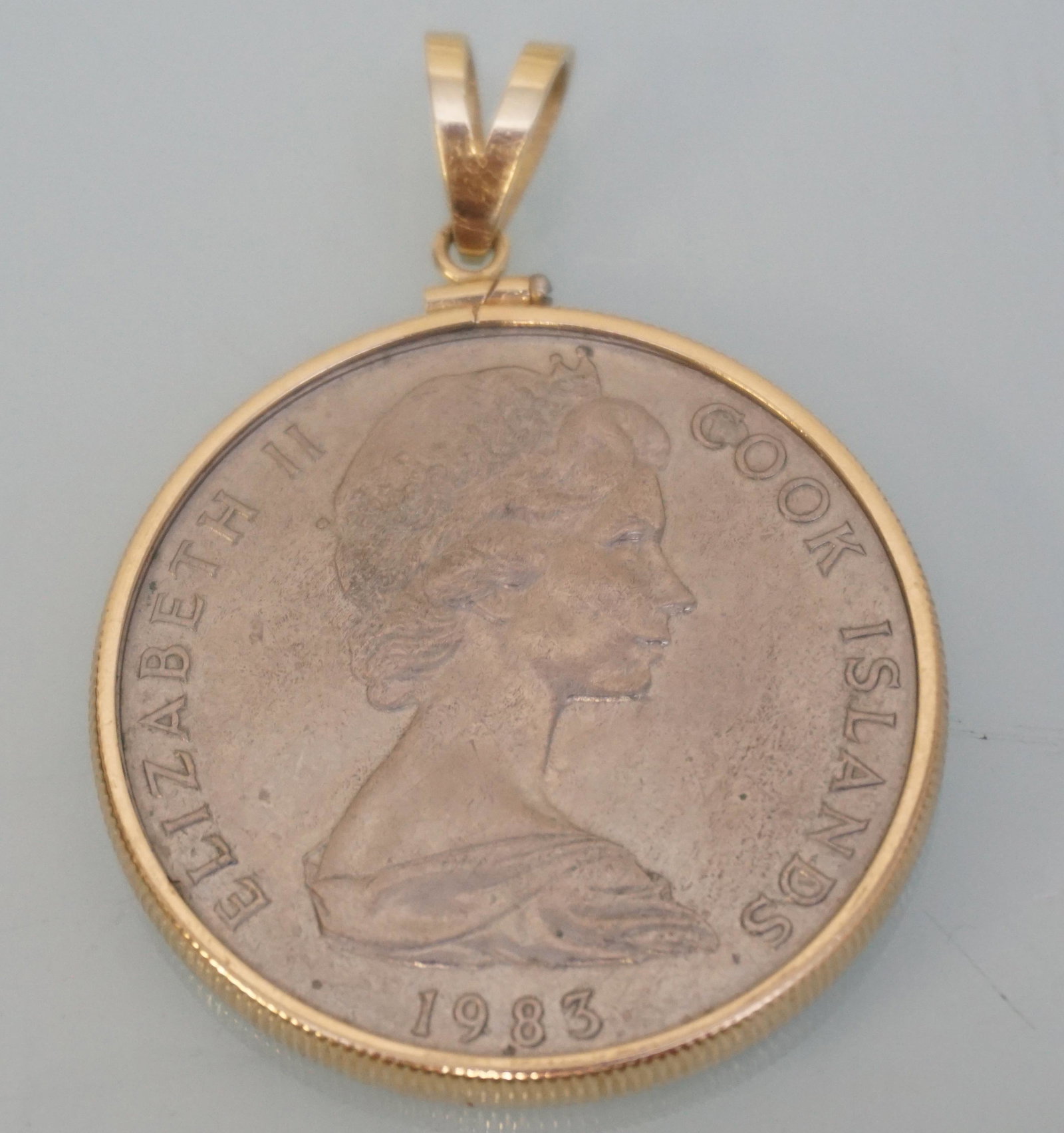 COOK ISLANDS 1 DOLLAR SET IN 14K PENDANT: 1983 Elizabeth II Cook Islands One Dollar Coin set in a 14k Yellow Gold Bezel to wear as a pendant. Measures 1 1/2". The reverse of this coin features Tangaroa, Polynesian God of the sea and creation;