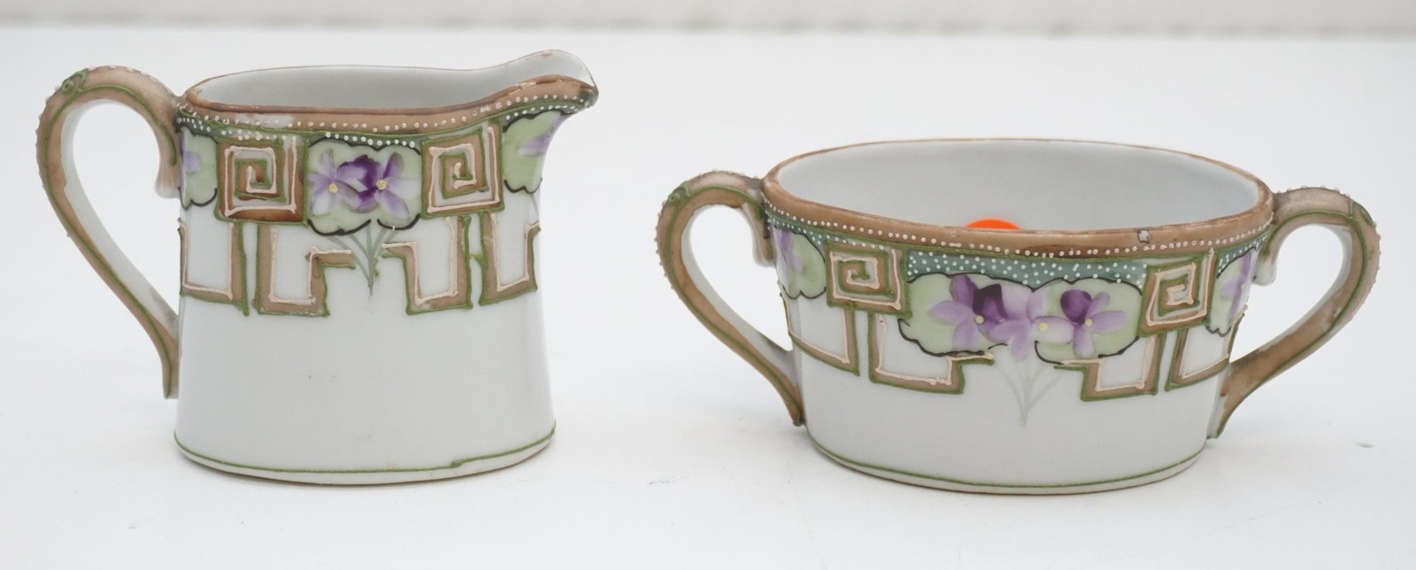 HAND PAINTED VIOLETS NIPPON CREAM & SUGAR: Antique Hand Painted and Enameled Violets Nippon Porcelain Cream and Sugar, Sugar 5 1/2" long. Creamer 3". Weight 10 oz. PROVENANCE: A Private Charleston SC Estate.