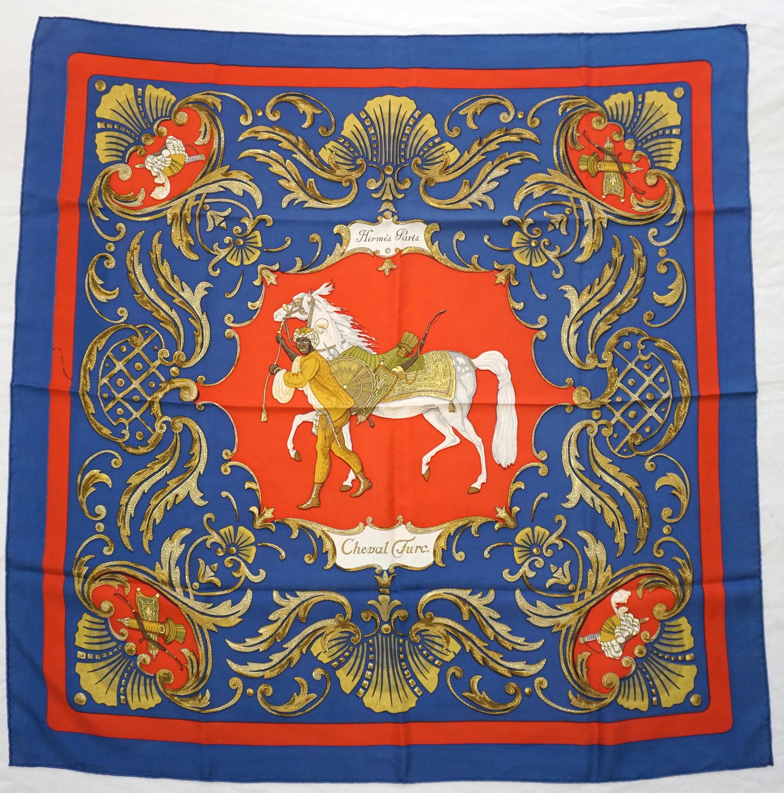 HERMES PARIS "CHEVAL TURC" SILK SCARF: Hermes Paris silk "Cheval Turc" silk scarf. The scarf is designed with a red central motif with a horse being led by an African character. The scarf is accented with gold scroll work and a rich purpli