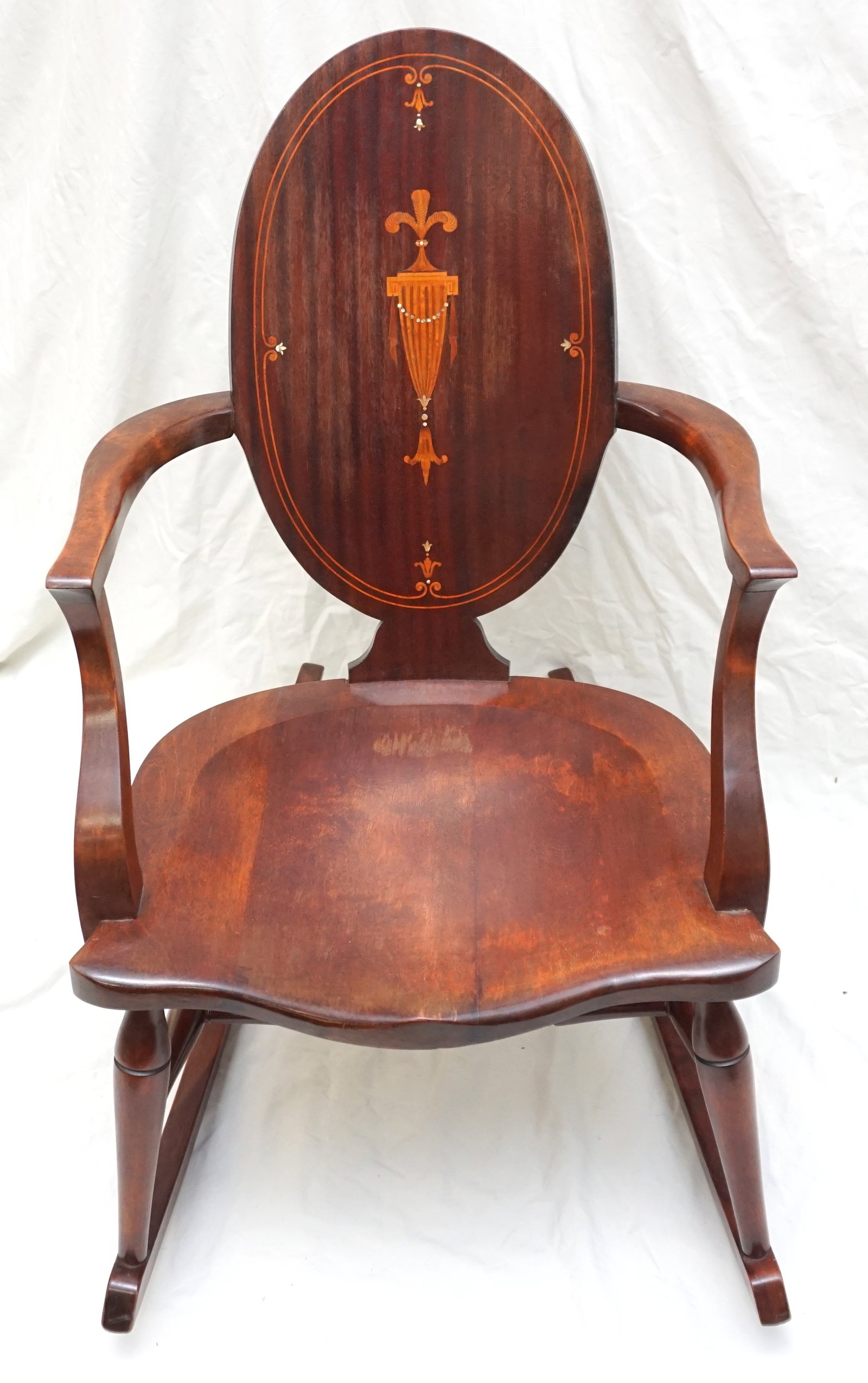 ANTIQUE INLAID MAHOGANY ROCKING CHAIR: Antique Mahogany oval back rocking chair. The back has an inlaid fruit wood urn design accented with mother of pearl and a double band along the rim of the back. The chair has age related wear as seen