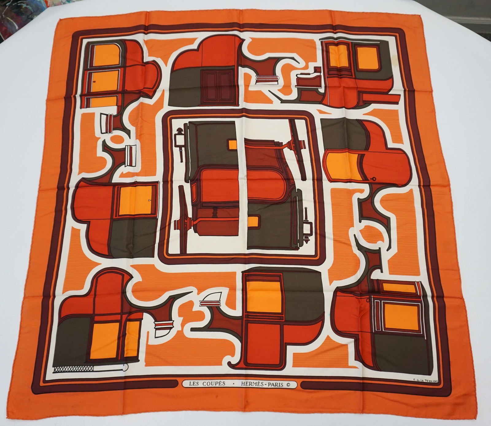 HERMES PARIS "LES COUPES" SILK SCARF: HERMES PARIS silk “les Coupes” scarf. This scarf features carriages as minimalistic shapes geometrically intertwined, in various shades of bright and muted orange, accented by dark taupe d