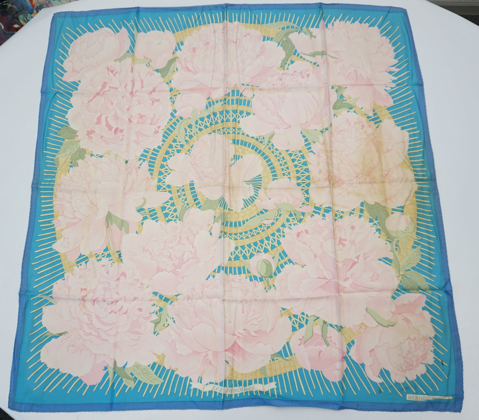 HERMES PARIS "LES PIVOINES" SILK SCARF: HERMES PARIS silk “les Pivoines” scarf. The scarf features graceful peony illustrations set against a backdrop resembling intricate canework. The scarf is in muted tones of pink and yellow
