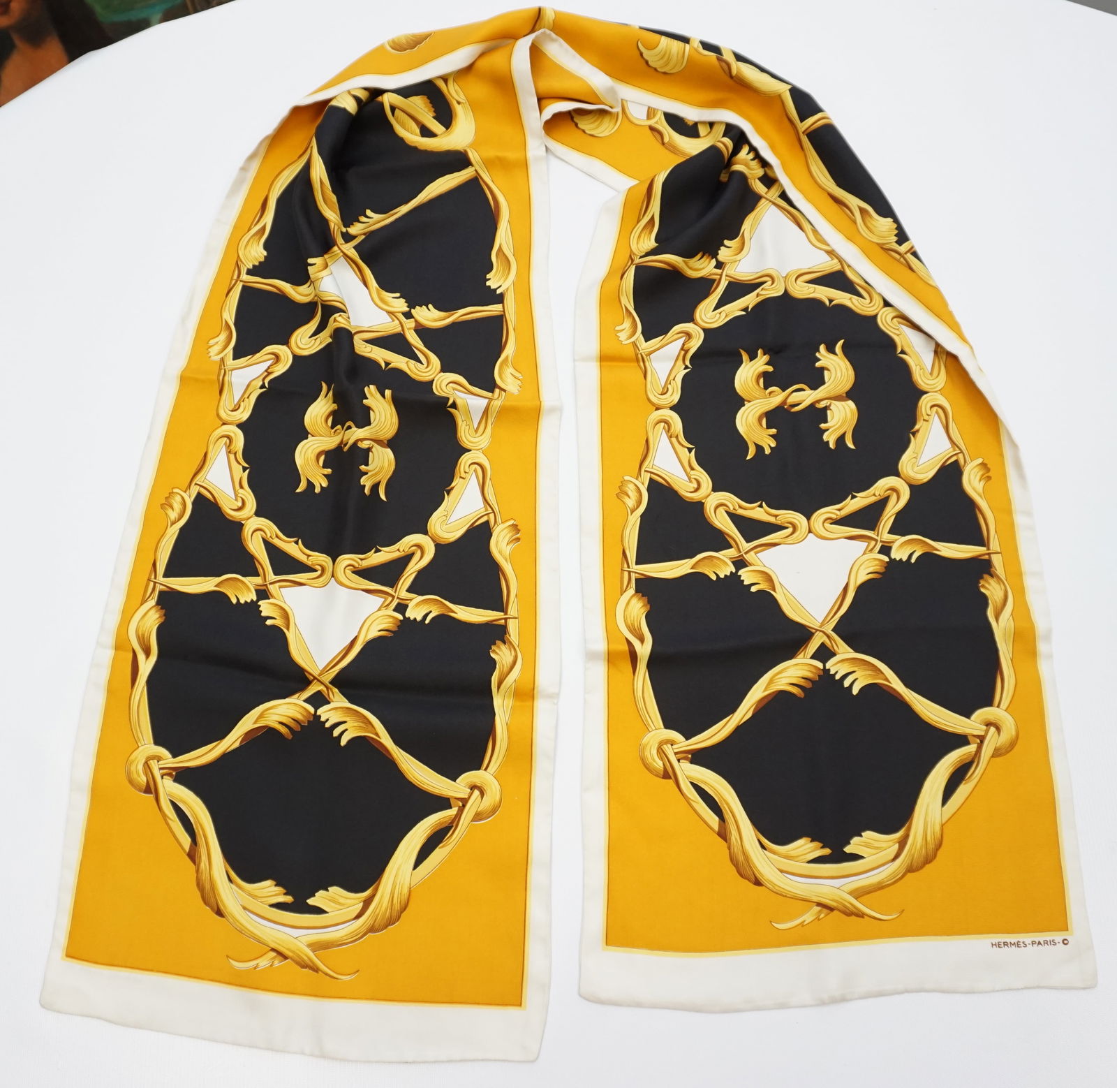 HERMES PARIS SILK SCARF: HERMES PARIS silk scarf. The scarf features ironwork in golden tones on both sides, over mustard cream and black background. The scarf measures approx. 72” x 13.25” Sewn in tag not present