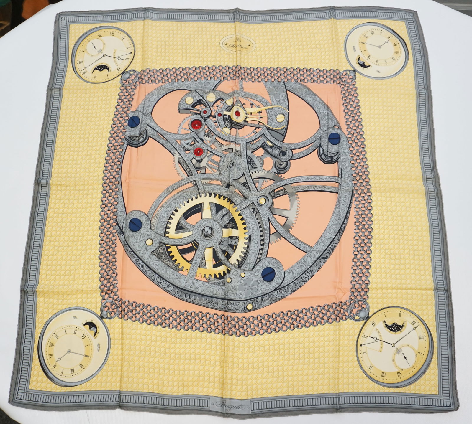 BREGUET SILK SCARF: BREGUET “Les montres” silk scarf featuring inside watch mechanisms at the center and pocket watches at each corner. Sewn in tag not present. The scarf measures approximately 35”