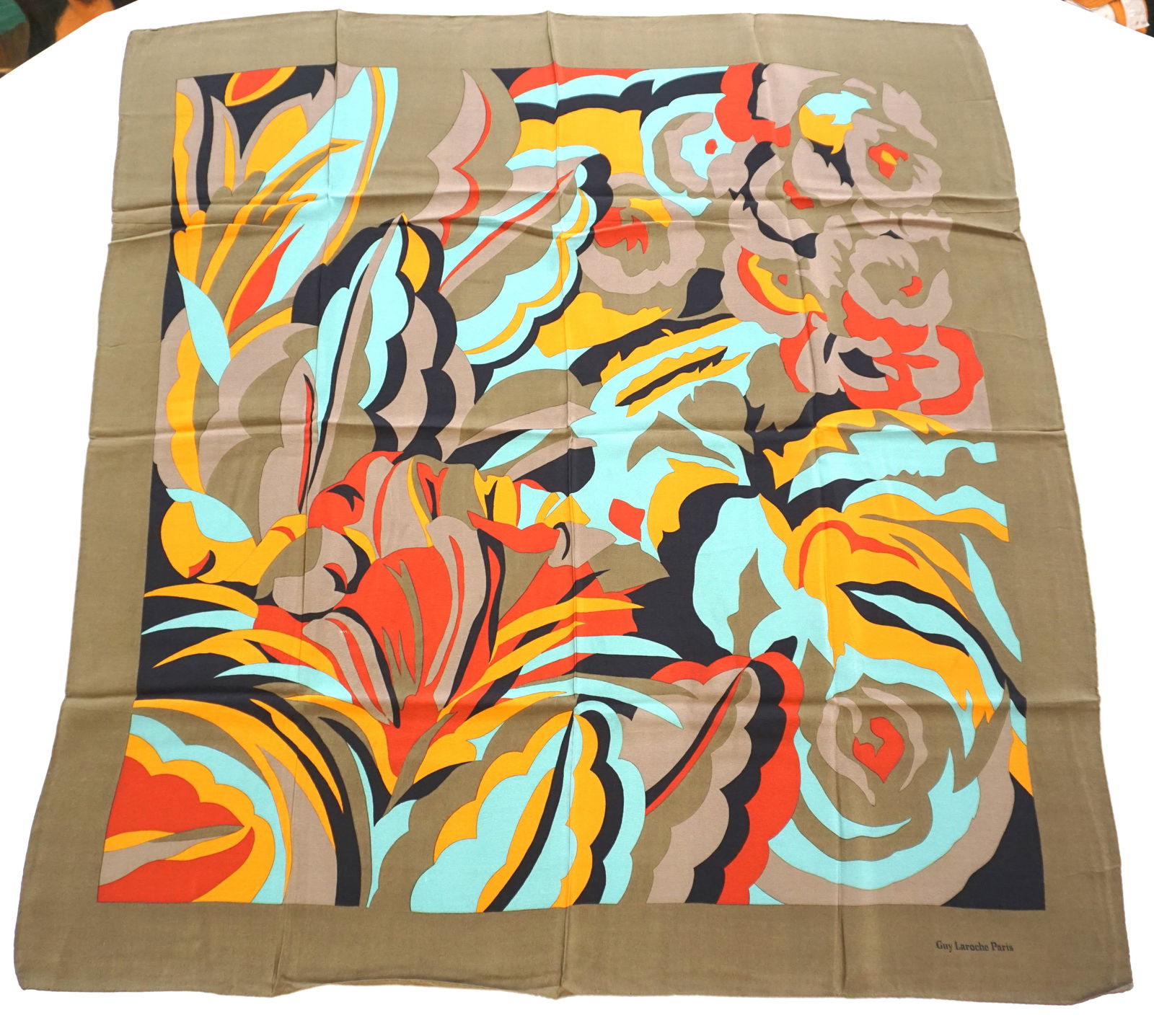 GUY LAROCHE SILK SCARF: GUY LAROCHE silk scarf featuring geometrical patterns in blue, brick, orange and taupe over a green background. Sewn in tag not present. The scarf measures approximately