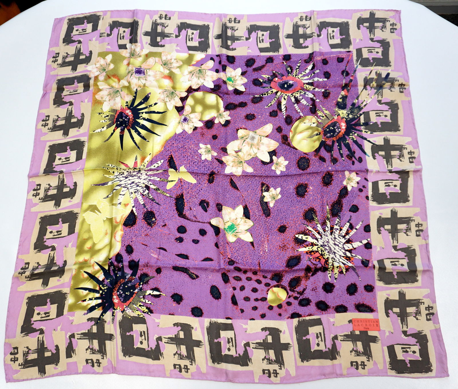 CHRISTIAN LACROIX SILK SCARF: CHRISTIAN LACROIX silk scarf featuring floral elements mixed together leopard prints and jewelry designs over a lavender background. Sewn in tag present. The scarf measures approximately