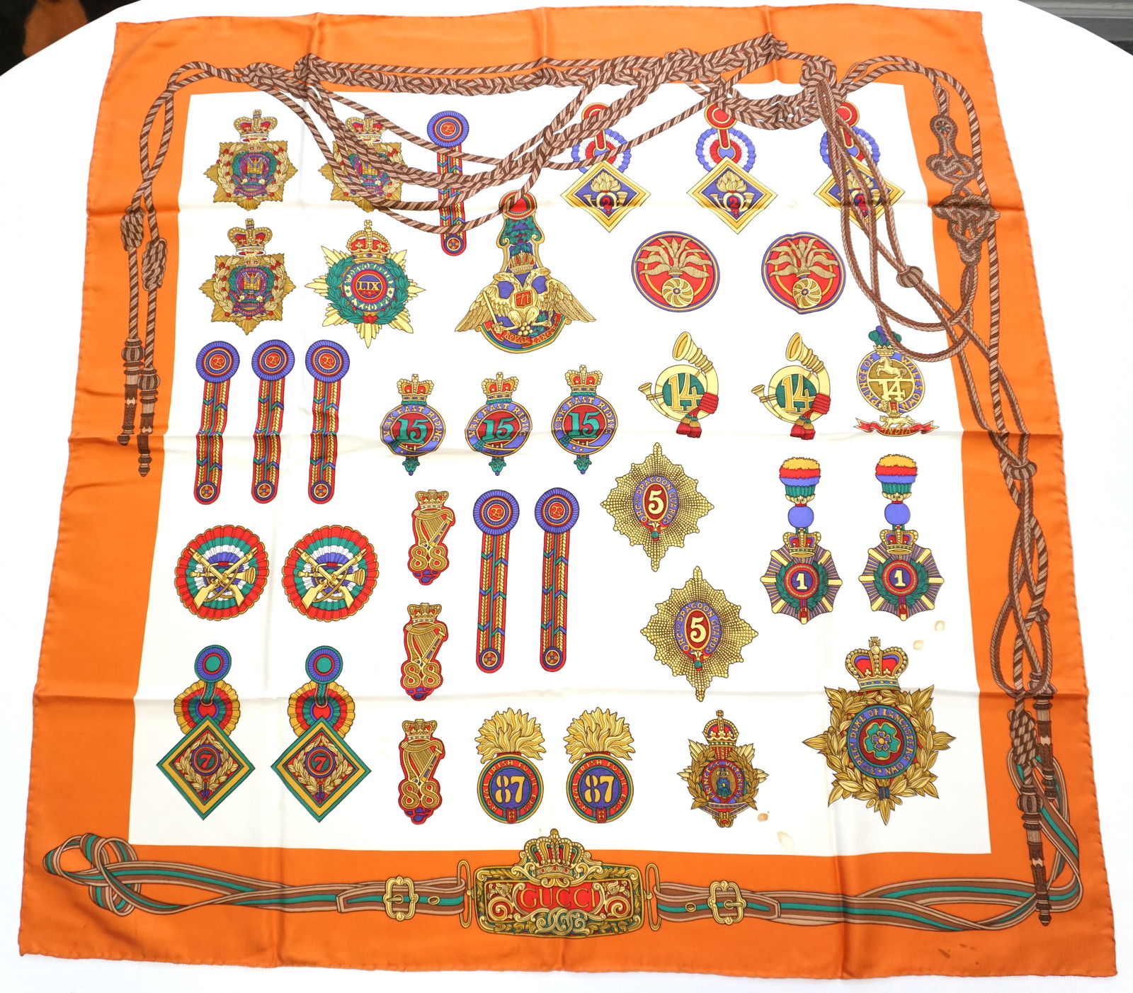 GUCCI ENGLISH AND IRISH MILITARY BADGES SILK SCARF: GUCCI Military badges silk scarf featuring varous English and Irish military badges over a white background with a deep orange border. Sewn in tag present. Rare, late 1960s. The scarf measures approxi