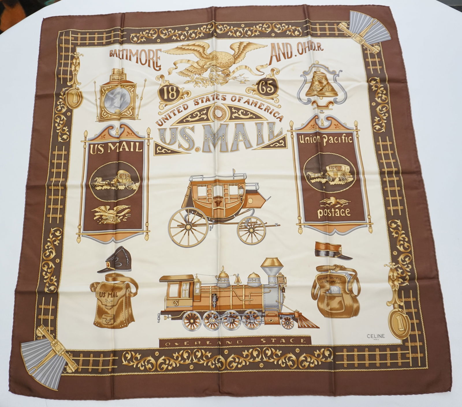 CELINE UNITED STATES OF AMERICA SCARF : CELINE “United States of America US. MAIL” scarf depicting various US Mail emblems in golden tones and various shades of brown accented with grey detailing. Sewn in tag not present. The sc