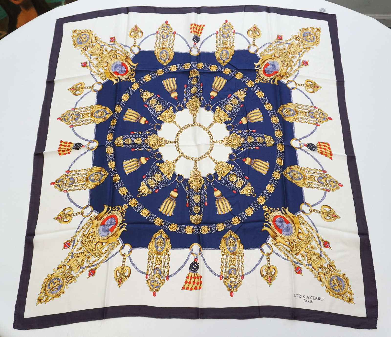 LORIS AZZARO SILK SCARF: LORIS AZZARO silk scarf featuring various jewelry elements from the 16th century accompanied by embroidery and tassels, over a white and dark blue background. Sewn in tag present. The scarf measures a