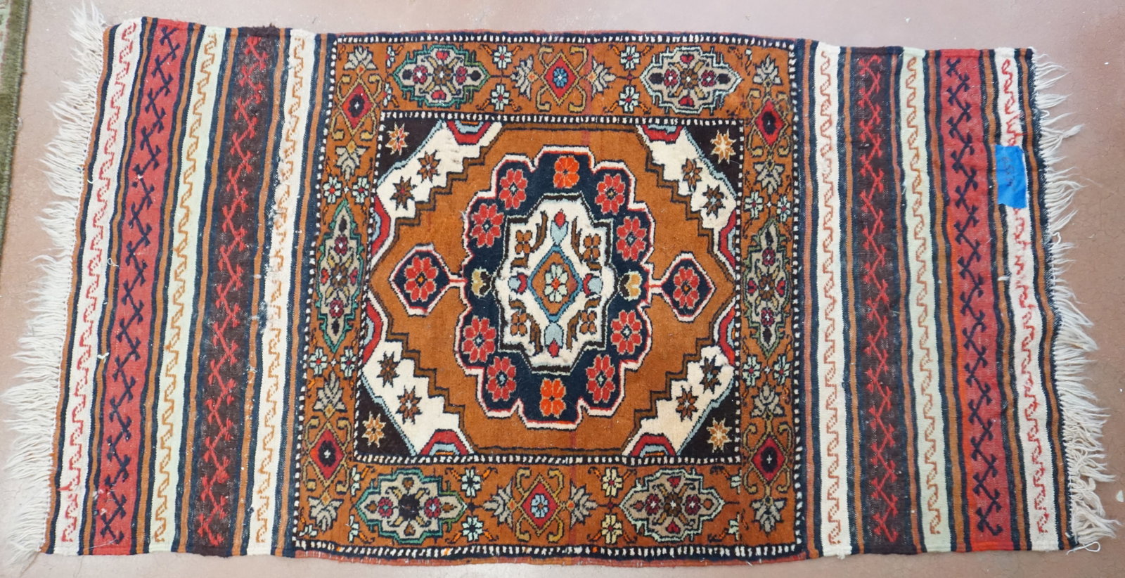 HAND WOVEN PERSIAN RUG: Hand made Persian rug, which perhaps could be transformed into a decorative pillow with the outer textile. The piece features a vibrant copper accented with white center with cascading tones of green,