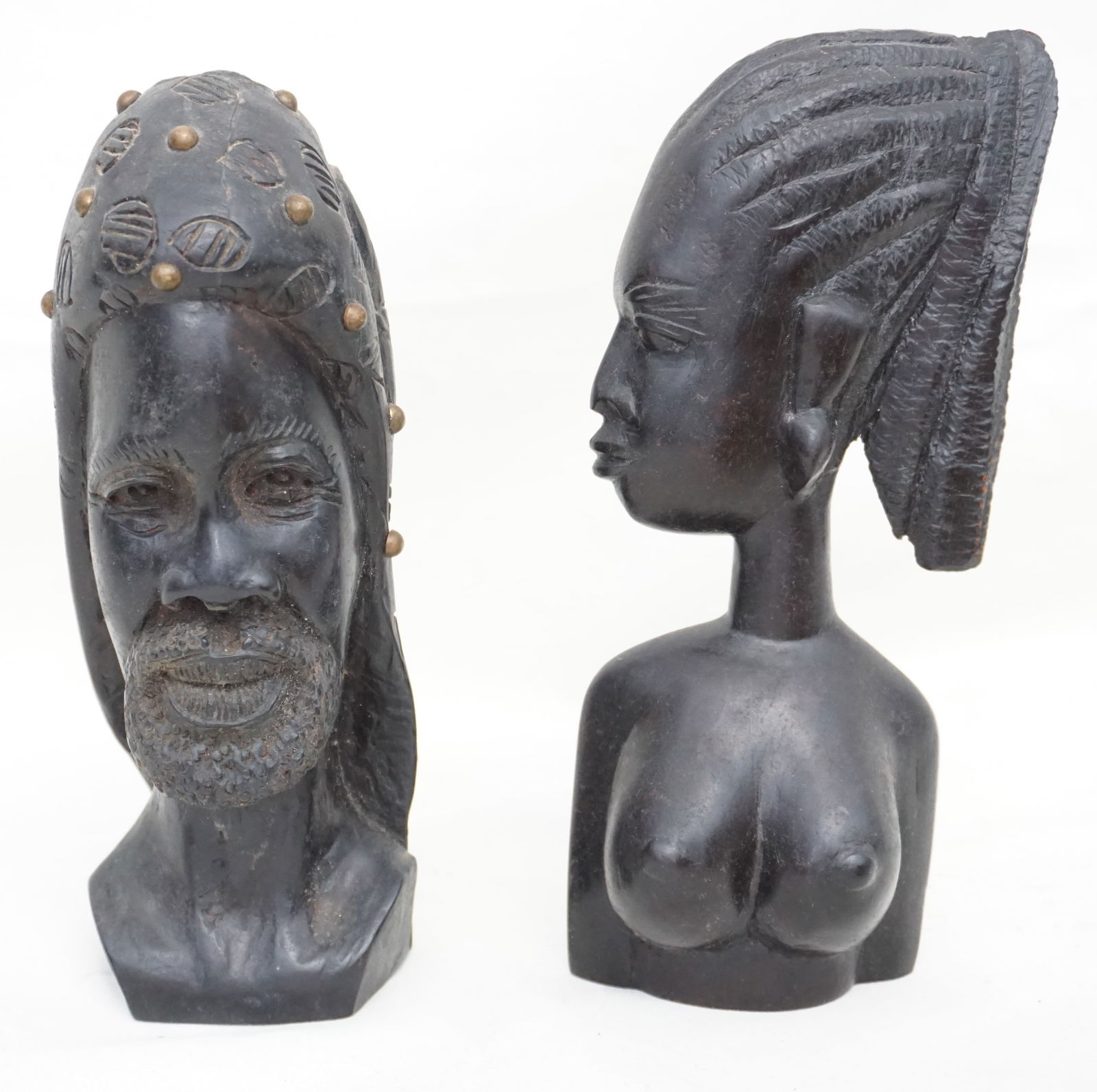PAIR CARVED MAHOGANY AFRICAN HEADS: Two African carved ebony figures. The male has a reverse of a tiger studded with brass. The female is nude with woven hair, both measure approx. 8" high, approx. weight 3lbs.