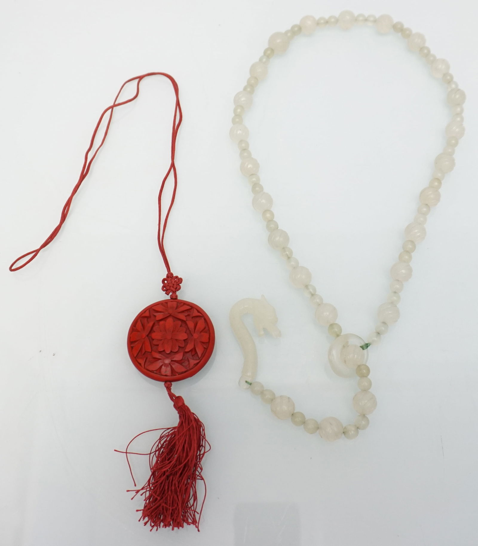 CARVED JADEITE NECKLACE & CINNEBAR PENDNT: This jewelry set includes a carved jadeite necklace and a cinnabar pendant. The jadeite necklace is 28" long and features a dragon-carved clasp, adding a unique and cultural touch. It is designed with