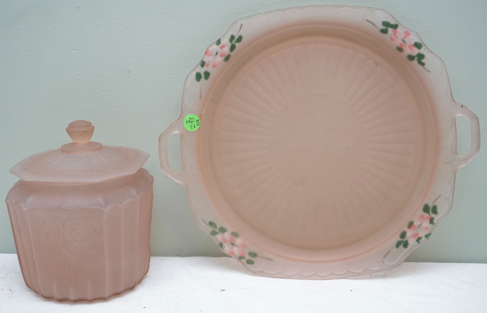 2 PC PINK GLASS TRAY & BISCUIT JAR: An elegant pair featuring a circular pink glass tray with a fluted edge, 14" in diameter, perfect for serving or as a centerpiece. Accompanying the tray is a matching biscuit jar, 7" in height, which