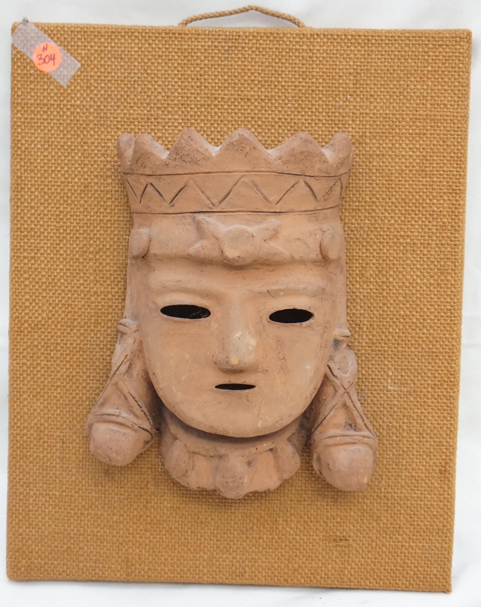 JAPANESE TERRACOTTA MOUNTED MASK: Mounted Japanese Terracotta mask "Ride of Ancient Culture". The mask features the head of a warrior and is mounted on a rectangular wood plaque covered in fabric. The piece measures 15x12" and weighs 