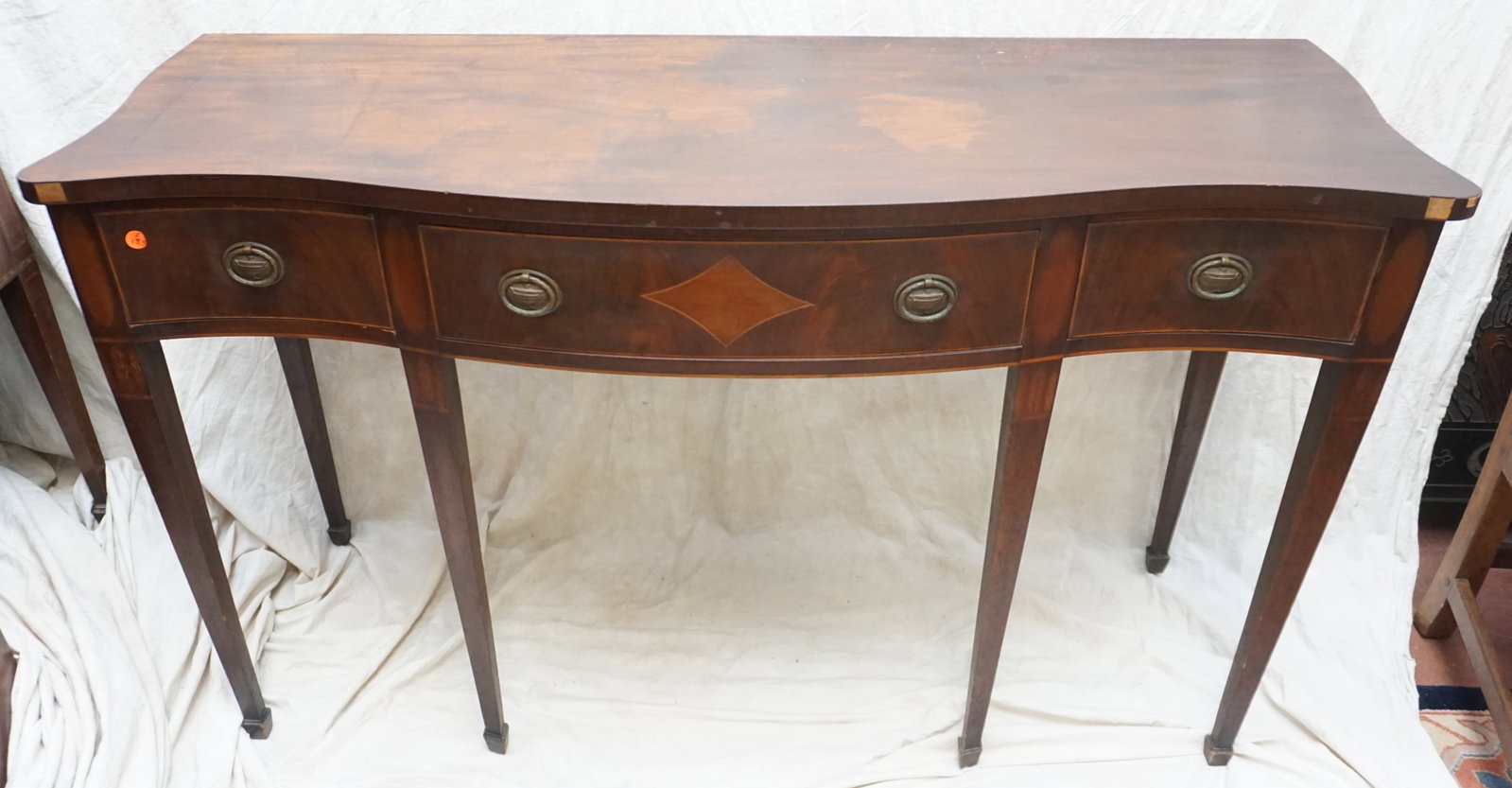 ANTIQUE MAHOGANY VENEER SIDEBOARD: The front of this antique mahogany veneer sideboard is adorned with three drawers, each featuring fine wood inlay that contrasts with the rich mahogany veneer. The top bears the history of the piece w