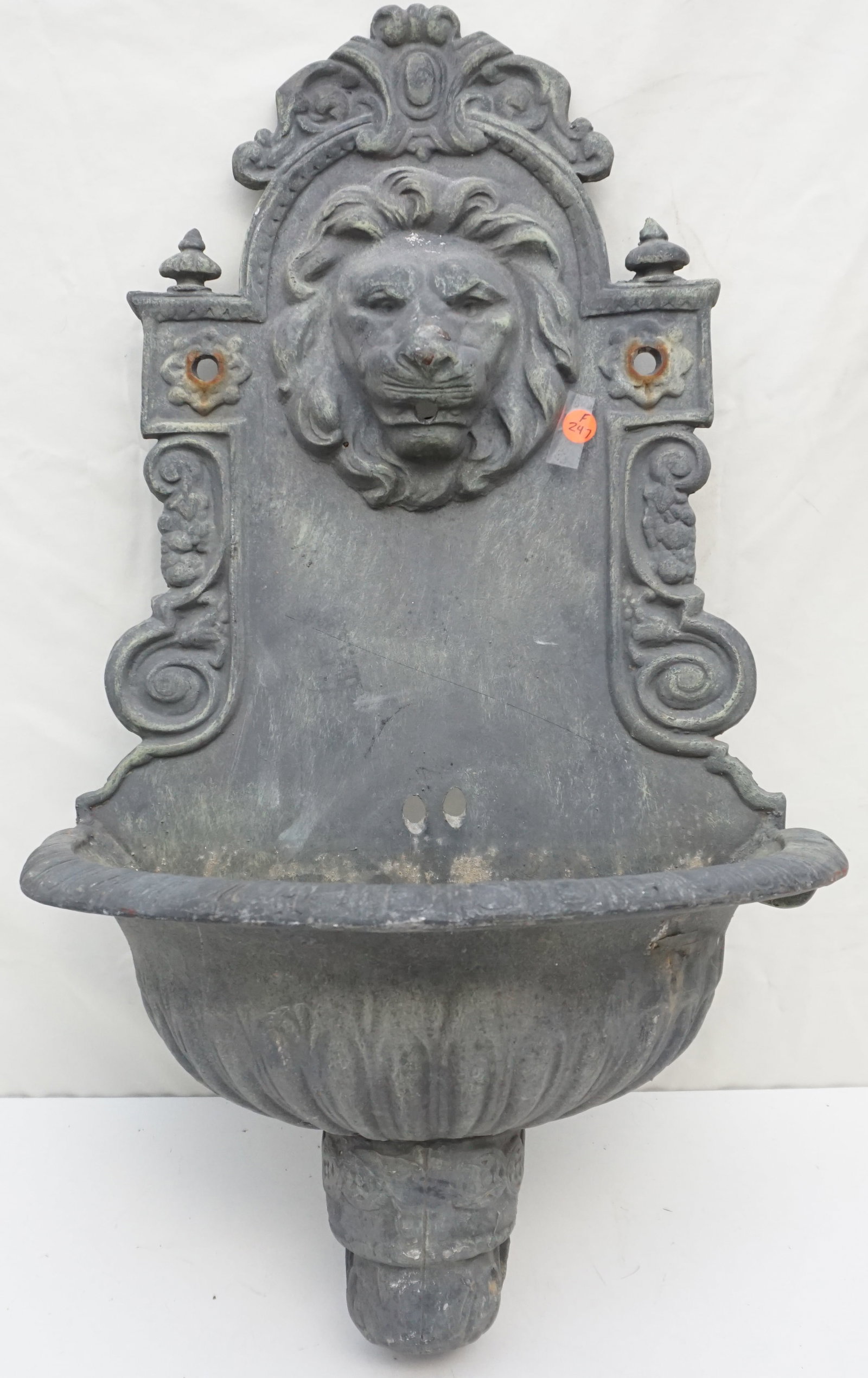 VINTAGE METAL WALL FOUNTAIN: The vintage metal wall fountain is an architectural salvage piece, rich with history and ornamental beauty. It features a central lion's head, a motif often associated with nobility and guardianship, 