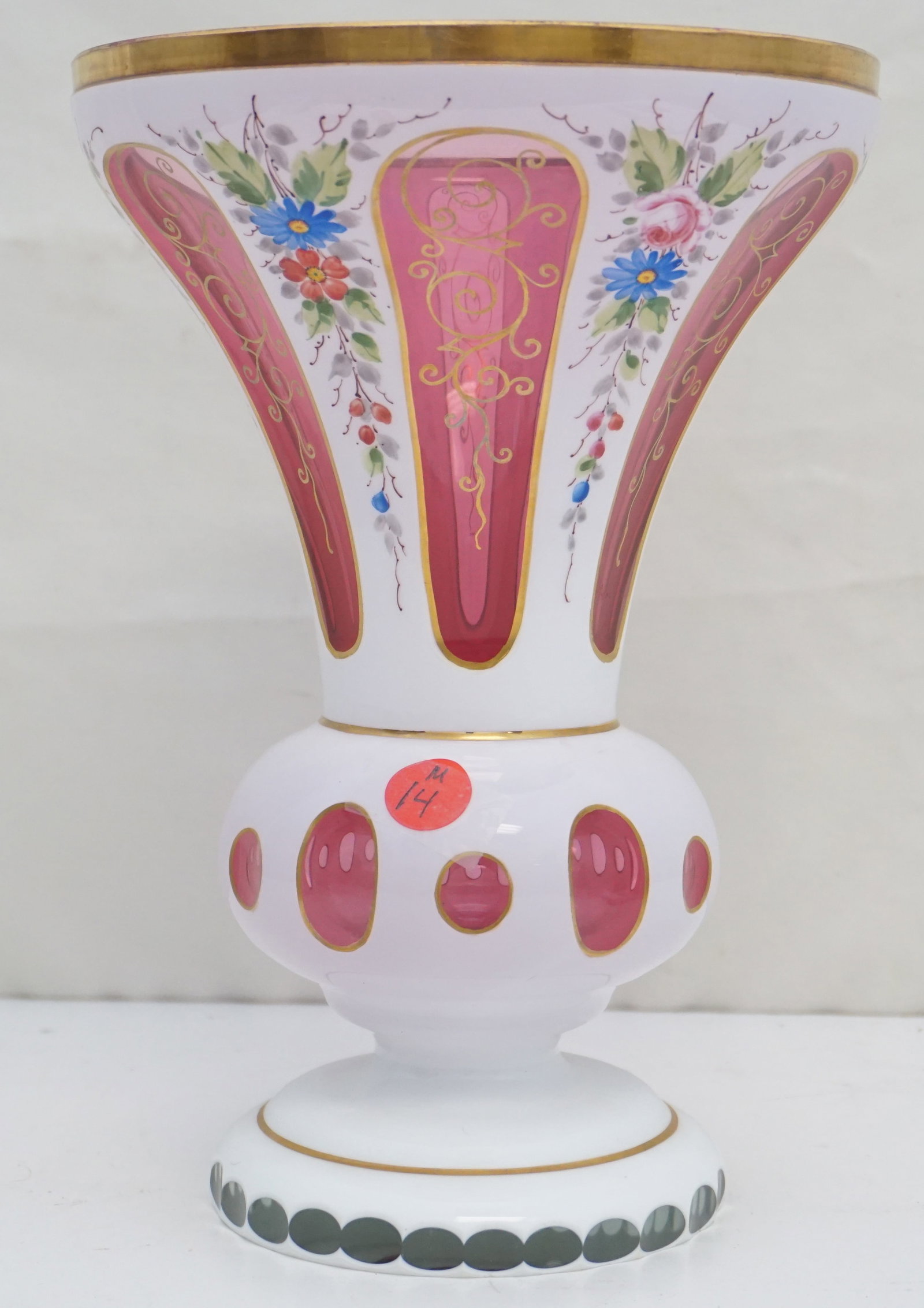 VINTAGE MILK CUT TO CRANBERRY GLASS VASE: This vintage Czech/Bohemian milk glass vase is masterfully cut to reveal a radiant cranberry hue beneath its milky translucence, adorned with hand-painted flower accents and a sumptuous gold rim. It s