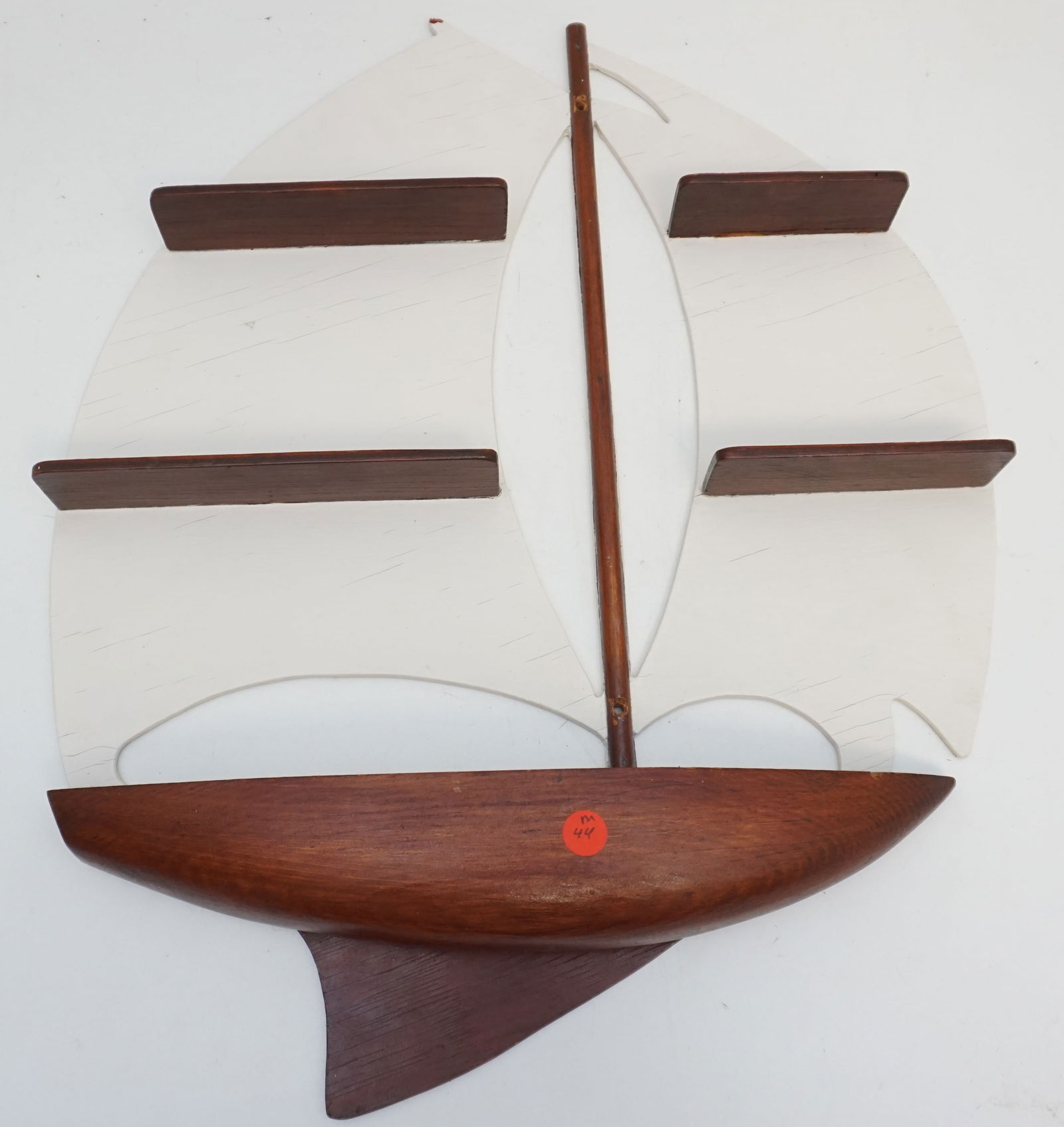 HANDMADE SAILBOAT DISPLAY SHELF: This is a creatively crafted display shelf, resembling a sailboat, with white painted surfaces emulating sails, intersected by stained wood masts. Its hull forms the base, providing stability and aest