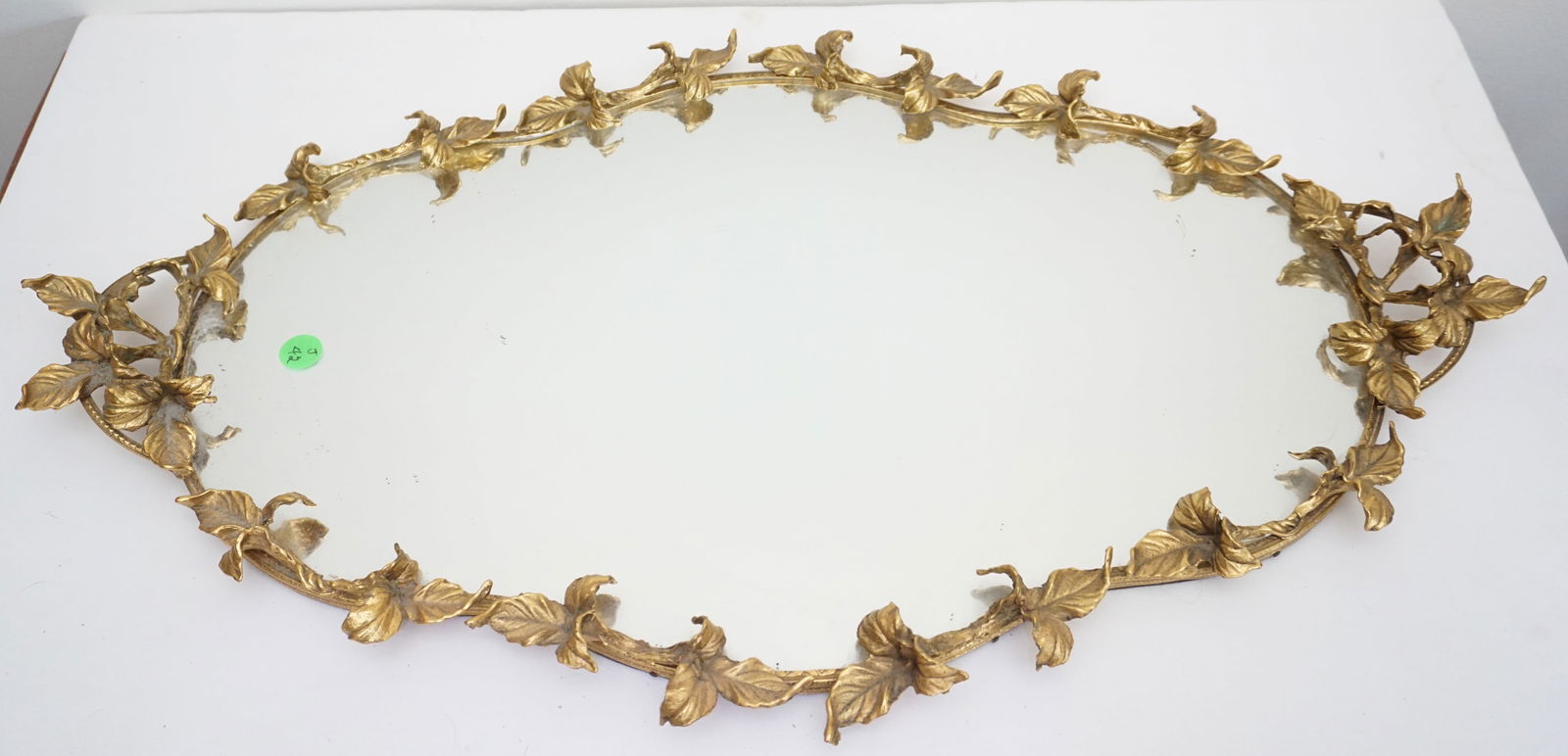 GOLD OVAL DRESSER MIRROR WITH LEAF DESIGN: This auction item features an exquisite oval dresser mirror with a beautiful gold-tone frame adorned with intricate leaf motifs. The elegant design adds a touch of nature-inspired charm and sophistica