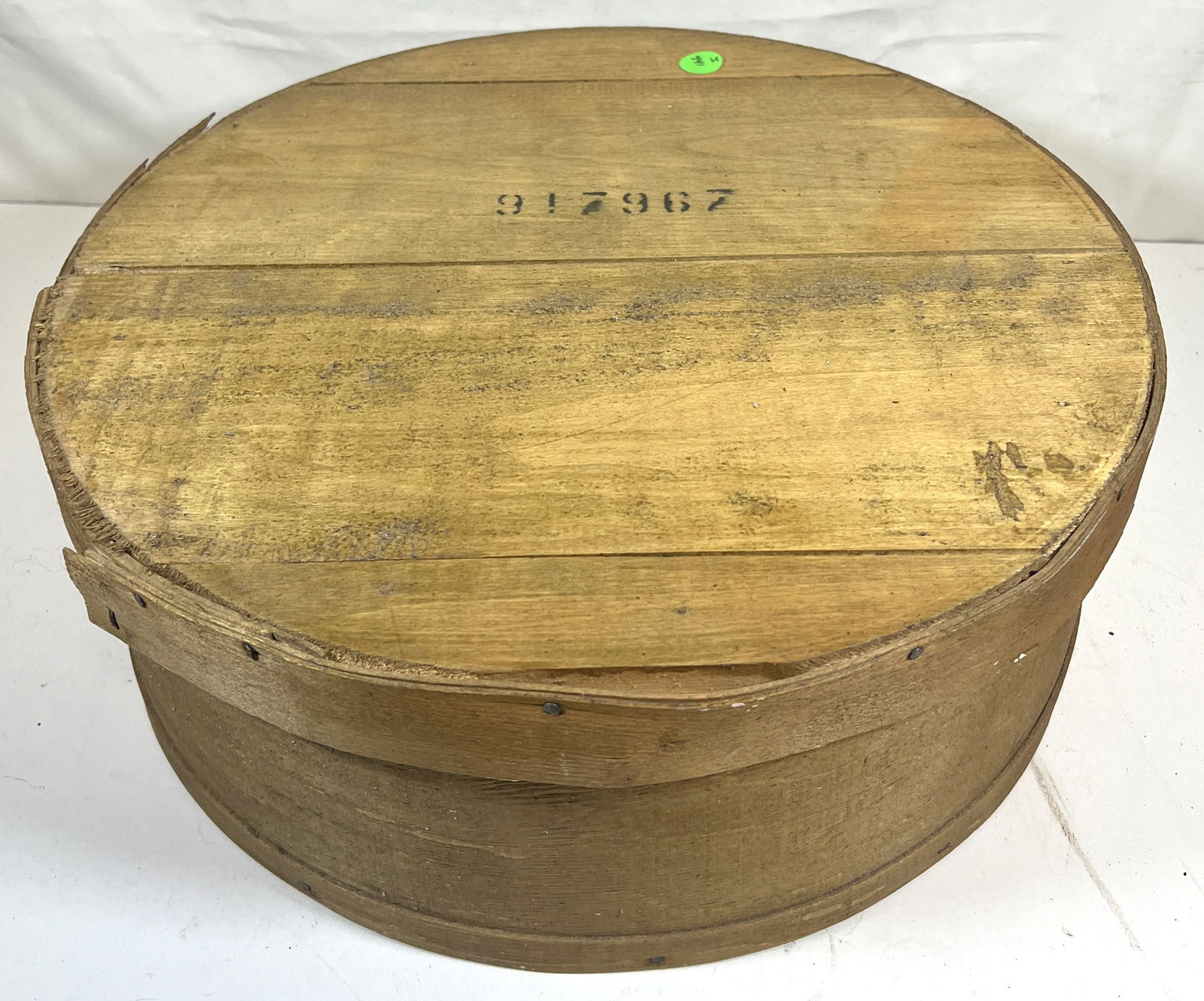 ROUND CHEESE BOX: Rustic round cheese box made from natural wood with a stamped "917967" on the lid. The box has a rough, unfinished appearance and is constructed with flat wooden slats and metal staples. The edges sho