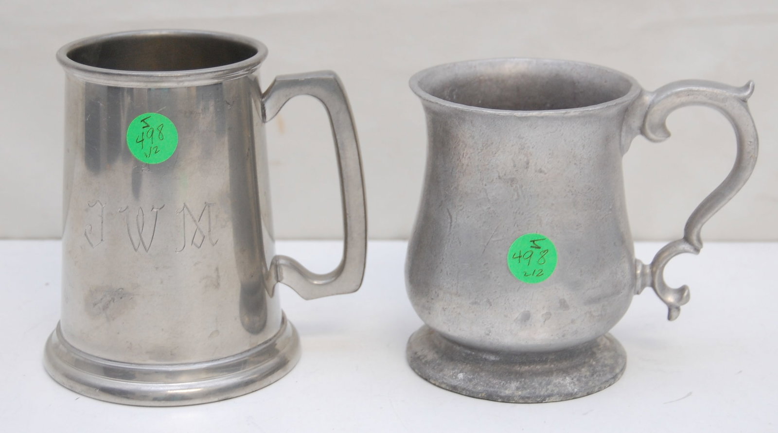 2PC METAL MUGS: 2-piece pewter mugs: 1 antique metal, standing at 4.75" high, and 1 Lunt mug with a glass bottom engraved with "JWM," standing at 5" high. Both pieces display a rustic charm with visible wear and pati
