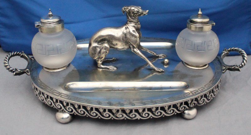 EDWARDIAN FIGURAL WHIPPET SILVER PLATE INK STAND: A fine English Edwardian figural silverplate ink stand. The sculpted figure of a whippet dog on footed oval base with carved Greek key border and matching etched glass ink wells. Length 14.5" x 8.75" 