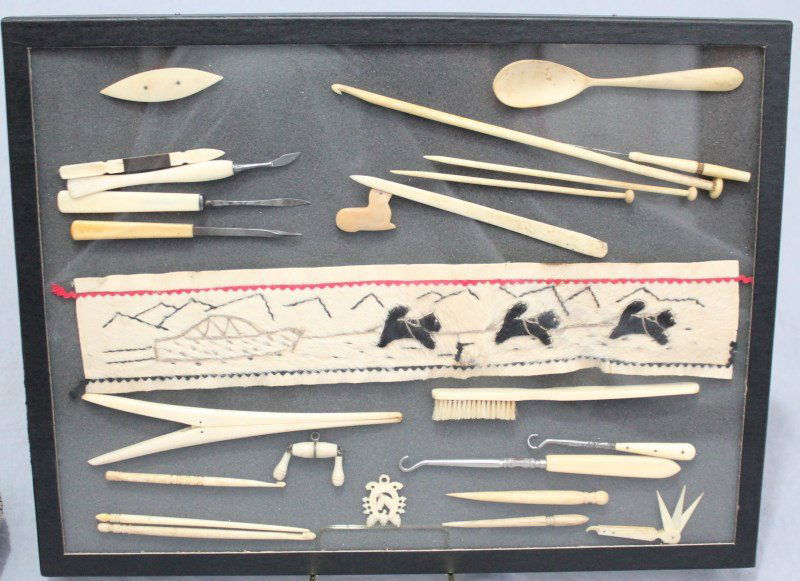 COLLECTION OF WHALE TEETH & BONE INUIT ART: A collection of carved whale tooth and whale bone and bone items from the 19th and early 20th c. There is a sealskin Inuit needlework piece featuring sled dogs. Several crochet hooks, bodkins, spoon,