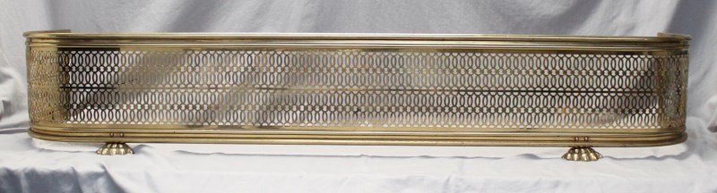 ANTIQUE BRASS PAW FOOT PIERCED BRASS FIREPLACE FENDER: Lion paw feet adorn this large pierced brass fireplace fender from the late 19th, early 20th century. The curved shape helped keep burning cinders from flying out onto the hearth. Provenance: A Charle