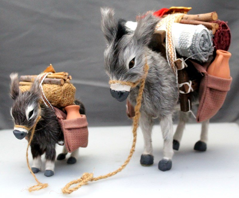 2 REALISTIC FUR BURROS FROM DUBAI: 2 Realistic Fur Burros from Dubai. With Dubai flags pins laden with firewood, rugs and terracotta pots. PROVENANCE: A Hilton Head South Carolina Private Collection. Larger 4x8x7. smaller 5x3.5x4. Wt 1