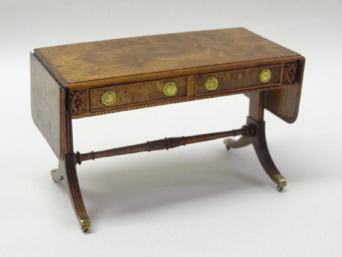 Thomas Warner Sofa Table Dollhouse Miniature: Thomas Warner regency style drop leaf sofa table, burl top with double drop-leaf, over two drawers and two faux drawers, Duncan Phyfe style base with brass caps and casters, 6.25"W opened, 4"W closed,