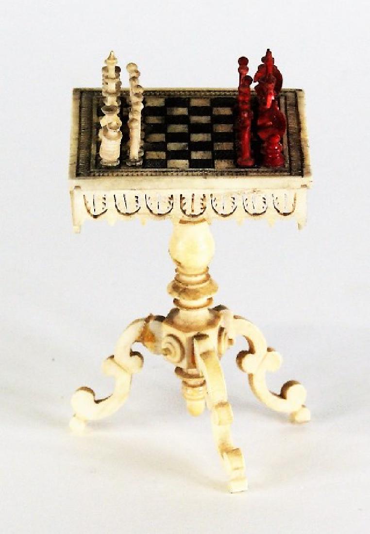 Antique Dollhouse Bone Chess Table Miniature: Antique carved bone chess game table with pierced apron, turned support and carved cabriole legs containing set of chess pieces, 1.5" square, 2.25"H to top of table