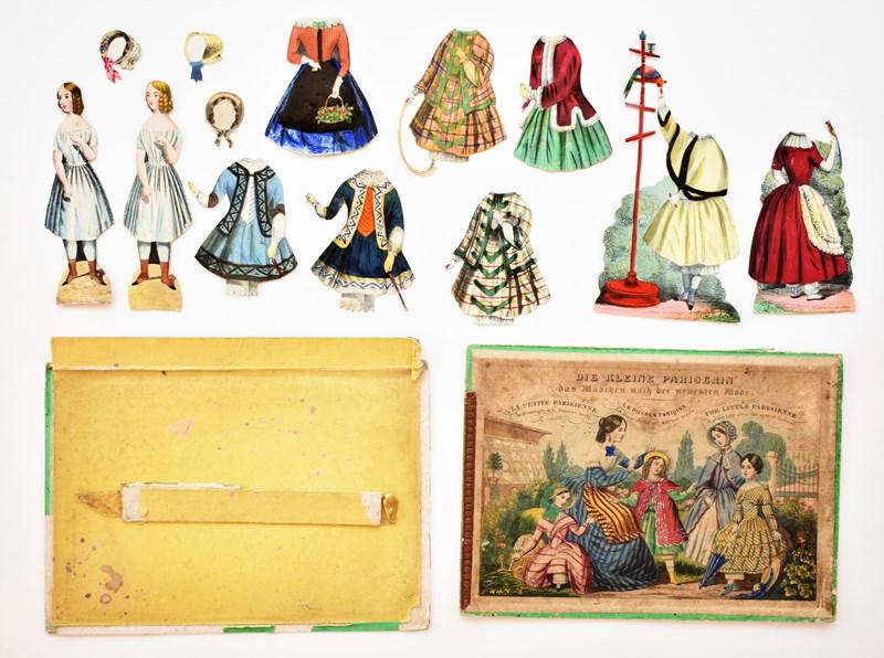 Die Kleine Pariserin Paper Doll Set: Mid 19th century Die Kleine Pariserin [The Little Parisenne] boxed paper doll set, two piece hand colored box printed in German, English, French and Italian 7" by 10" with losses and missing flaps has