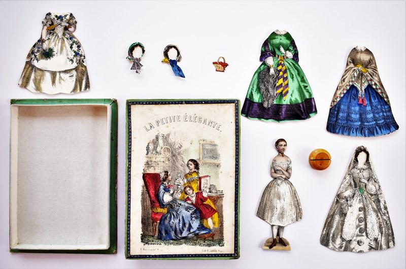 19th Century French Paper Doll Set: 19th century French boxed paper doll set, hand colored two piece box 4.5" by 6.25" in very good condition has a front and back doll 4.5"H with neck repair, wood stand, front and back wedding gown, 3 f