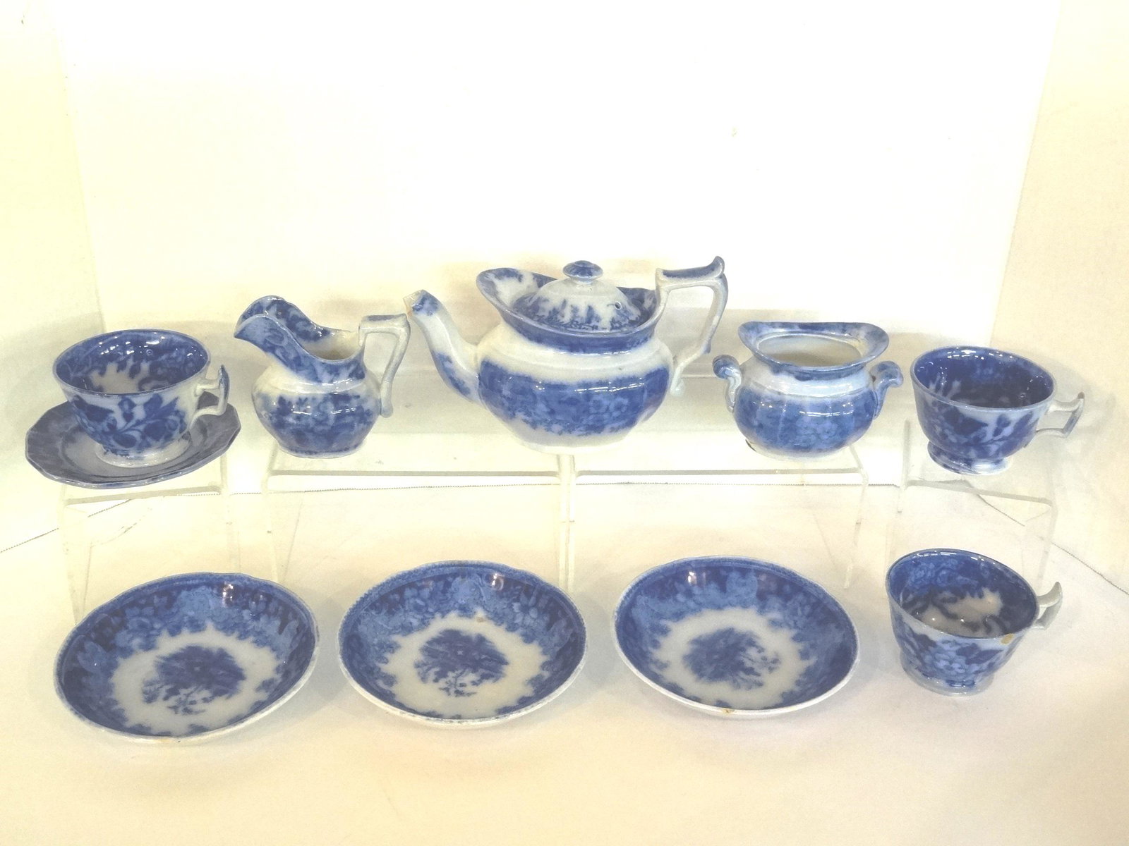 Flow Blue Shanghai Child's Tea Set: Antique flow blue child's tea set in the Shanghai pattern, marked with a W inside a diamond, teapot 7"L with chipped spout, open sugar bowl with small hairline, creamer, 3 teacups with 1 rim chip, sau