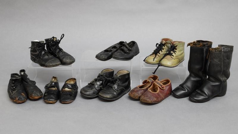 Eight Pairs Children Shoes: A group of dark colored children shoes, 3 buttons, one boots & others, show wear, some colored