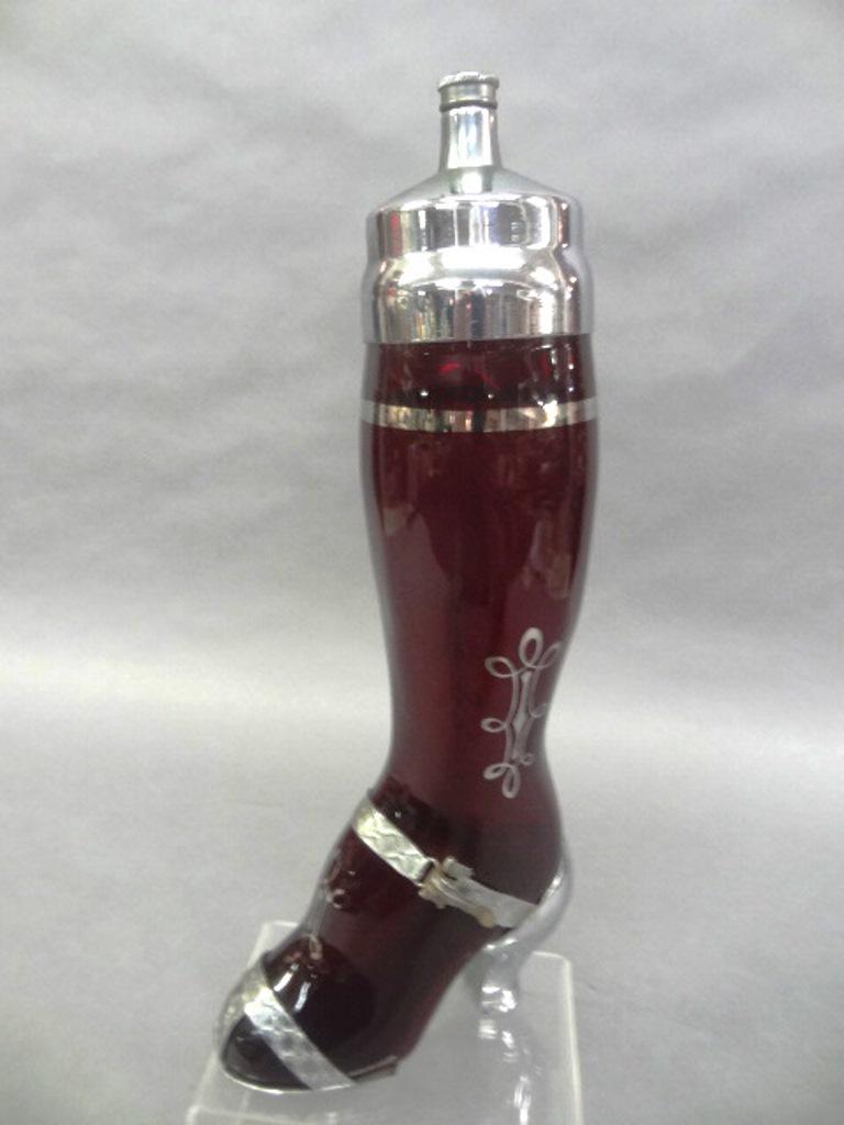 West Virginia Glass Leg Martini Shaker: Ruby glass lady's leg cocktail mixer with chrome plated top, silver overlay band and scroll and an aluminum shoe with chrome heel 15"H, circa 1935, attributed to the West Virginia Glass Specialty Co.