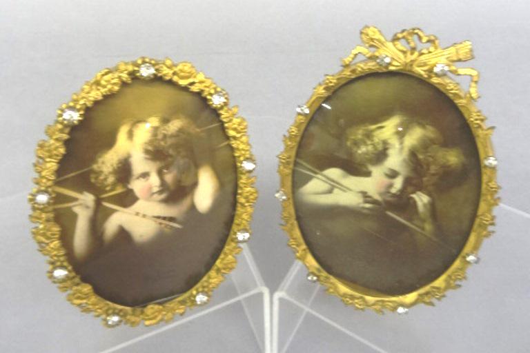 M.B. Parkinson Cupid Awake & Asleep Prints: Pair of prints by M.B. Parkinson copyright 1904 depicting Cupid Awake and Cupid Asleep, housed in a pair of plated easel back frames with ormolu and rhinestone edging, 3.5" by 5.5"