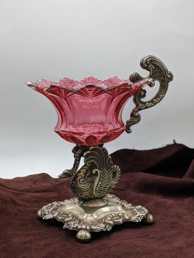 Antique Cranberry Glass Swan Compote: Antique cranberry glass compote with a scalloped edge mounted onto a silver-plate swan form base with a matching handle, 6.25"D bowl, 8.75"H