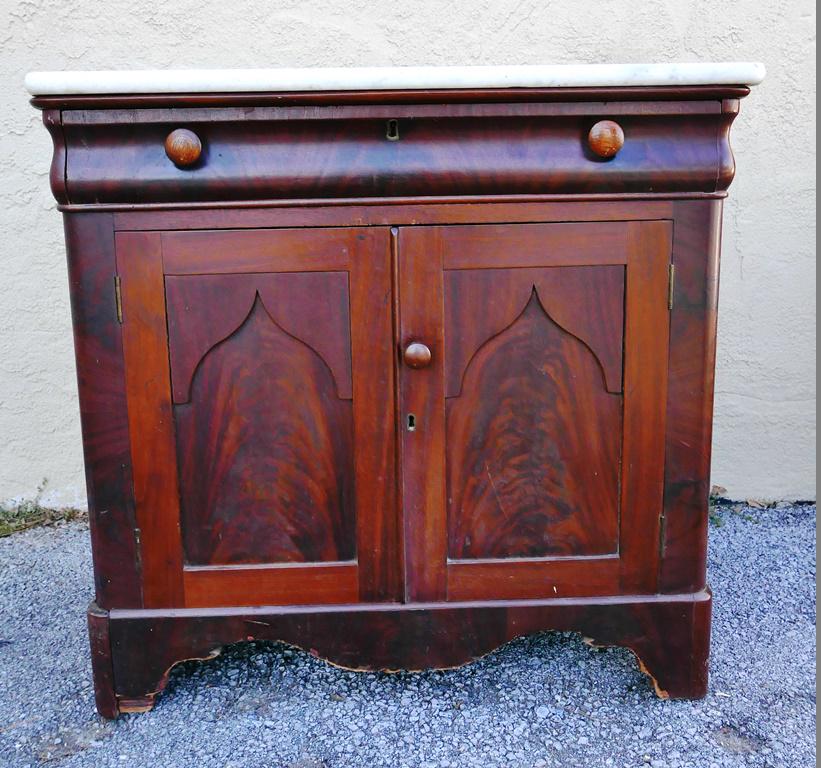Pa. Marble Top Wash Stand: Late 1800's Pa. marble top wash stand, base has highly figured mahogany veneer, single curved drawer over double arched paneled doors covering one shelf, deeply scalloped skirt, 31"W, 17.5"D, 29.5"H