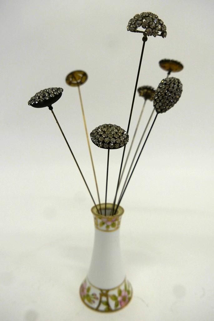 Seven Antique Hat Pins & Nippon Stand: Group of seven antique hat pins and a hand painted Nippon hat pin holder 4.75"H, enamel over gold gilt sterling pin depicting a state of city seal 12.5"L, group of 6 pins with glass paste stones, larg
