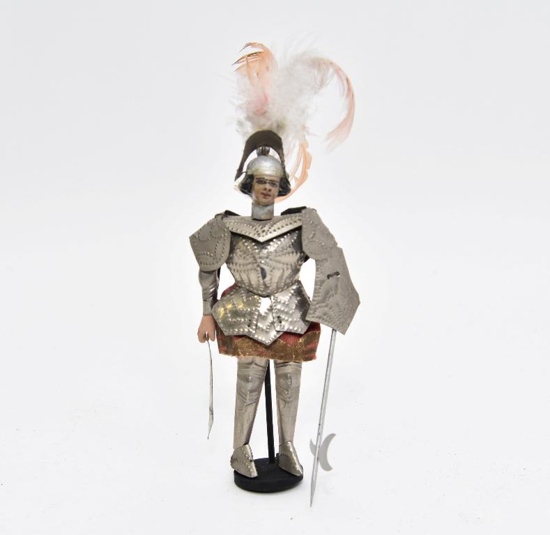 Vintage Dollhouse Knight Suit Of Armor: Vintage doll has a composition head over a wood jointed body, tin jointed armor with a feathered plume, fabric coat with Dresden paper trim, 7"H excluding feather
